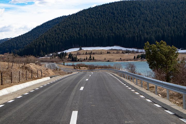 a road with a body of water and trees in the background